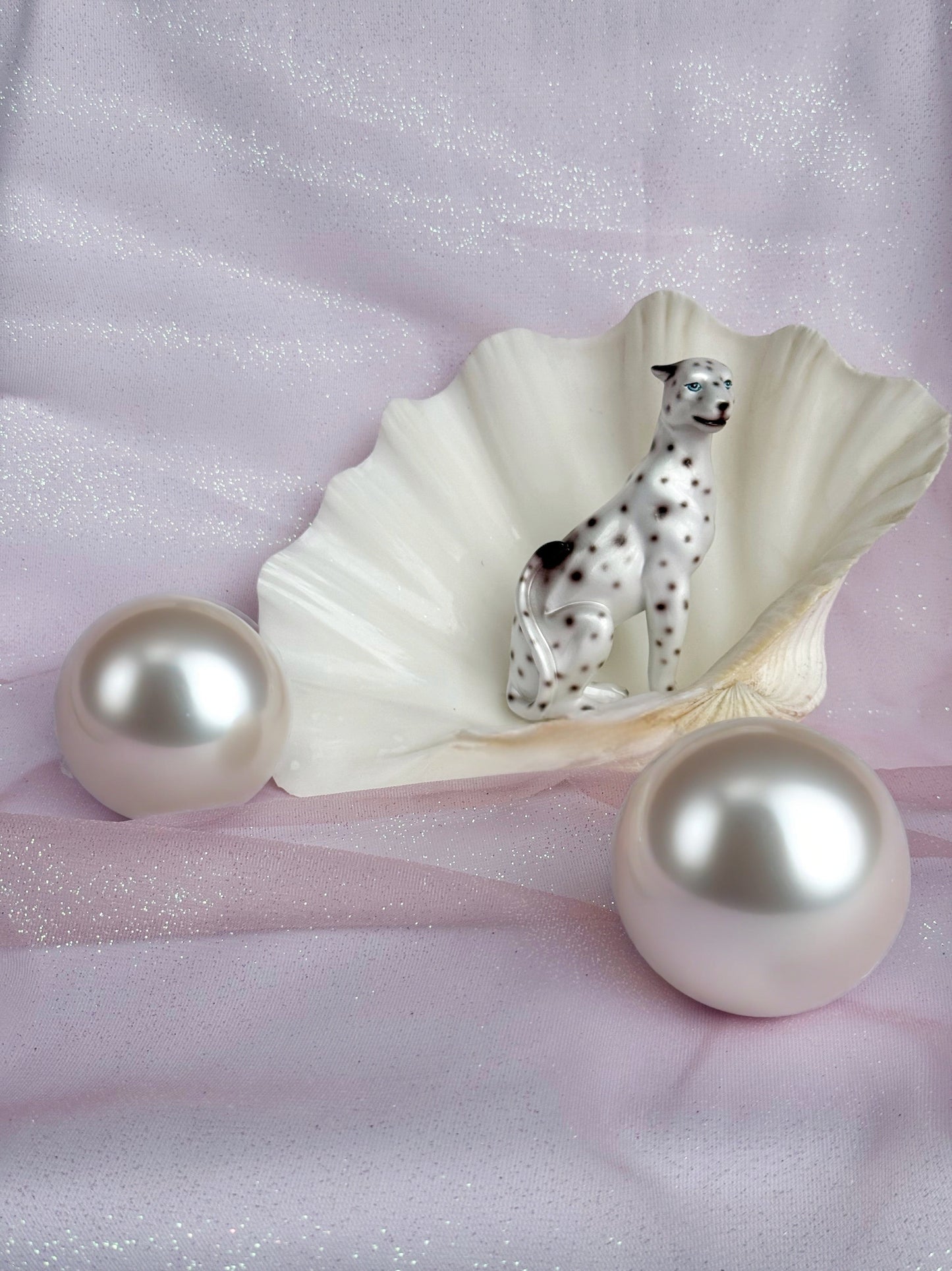 Decorative shell with a white leopard figurine, pearl-like spheres on a pink fabric background