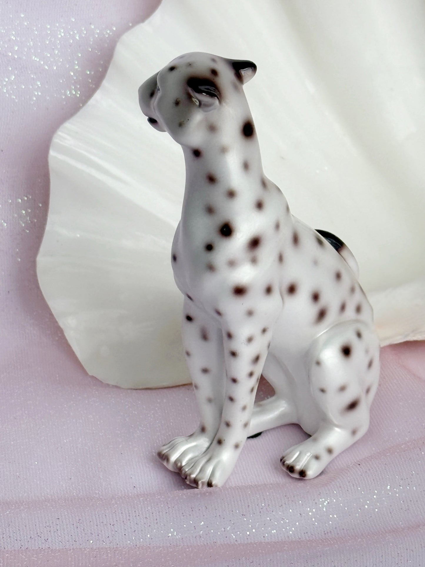 White resin figurine of a leopard with black spots on a pink surface