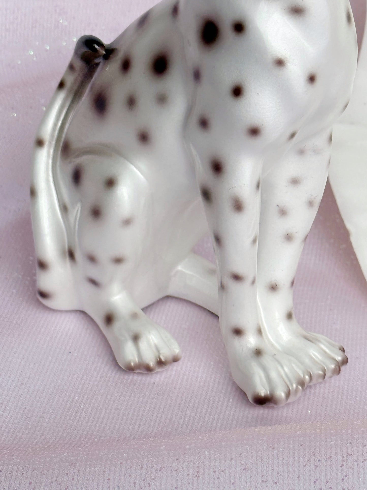 White ceramic leopard figurine with brown spots on a pink background