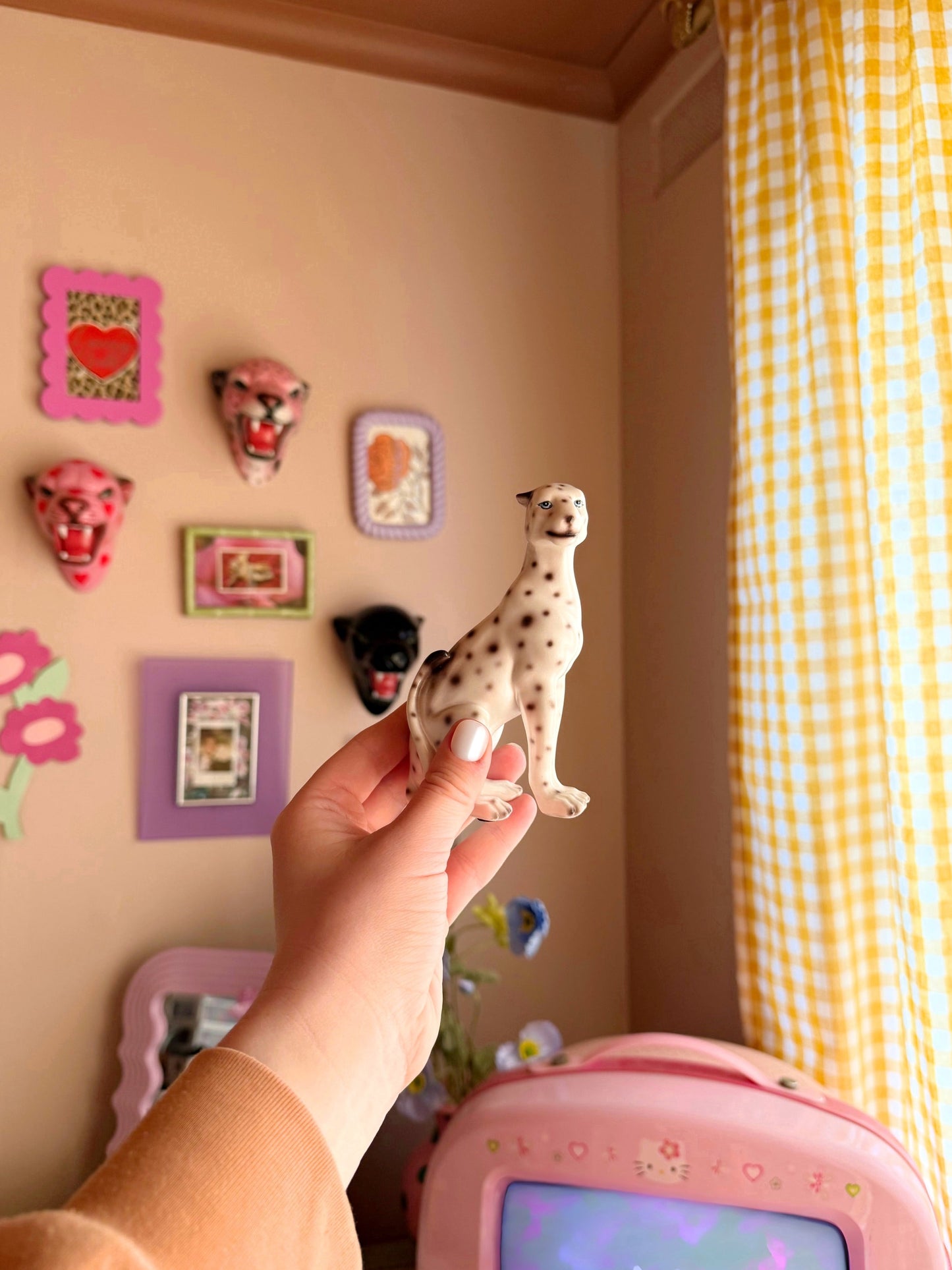 a hand holding a mini white leopard figurine with colourful home decor in the background