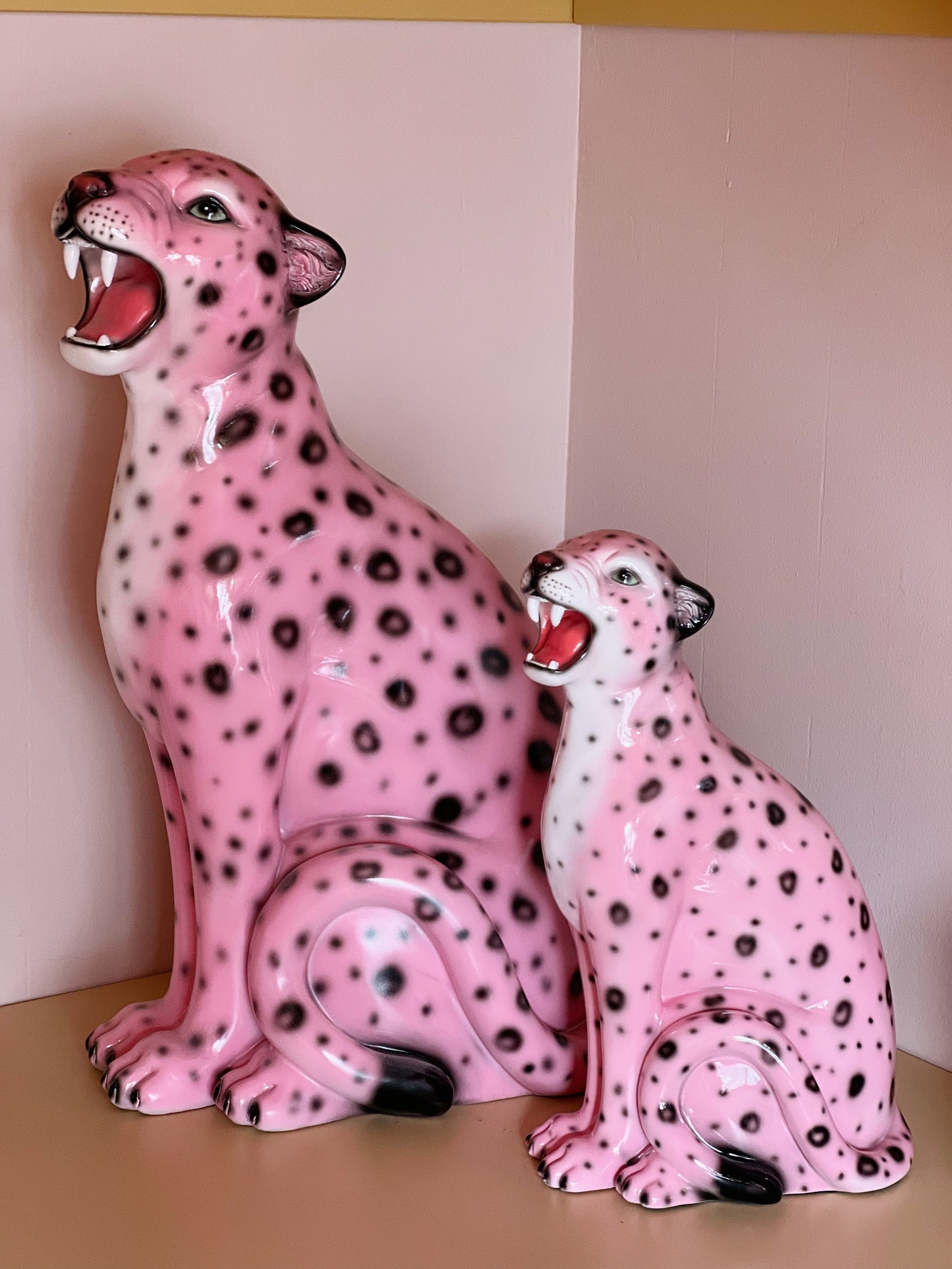 Two pink ceramic cheetah figurines with black spots on a beige surface.