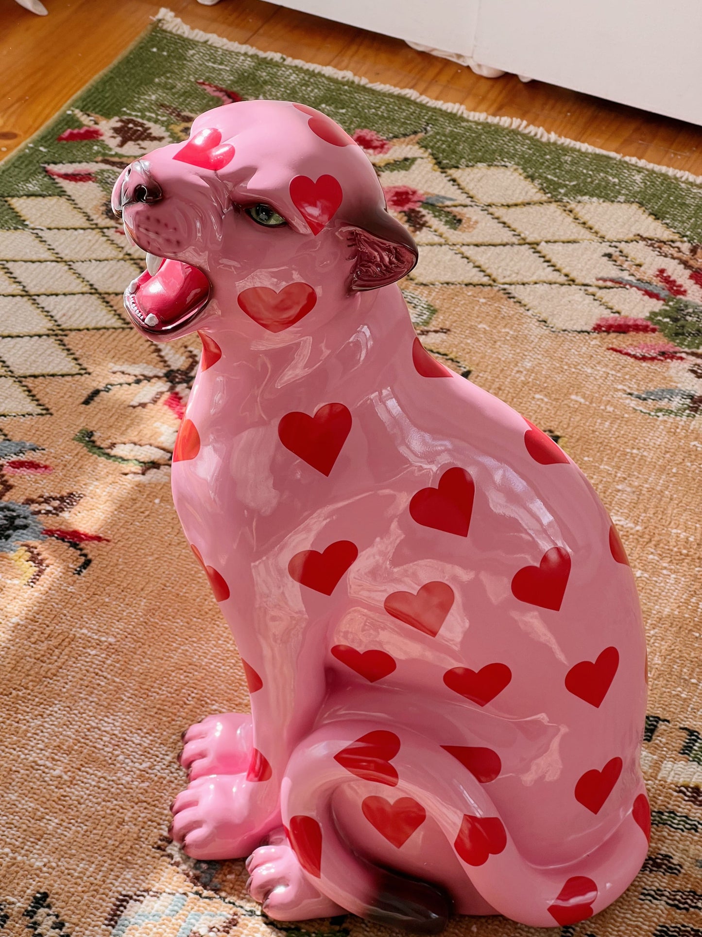 Pink resin leopard figurine with red heart patterns on a patterned rug