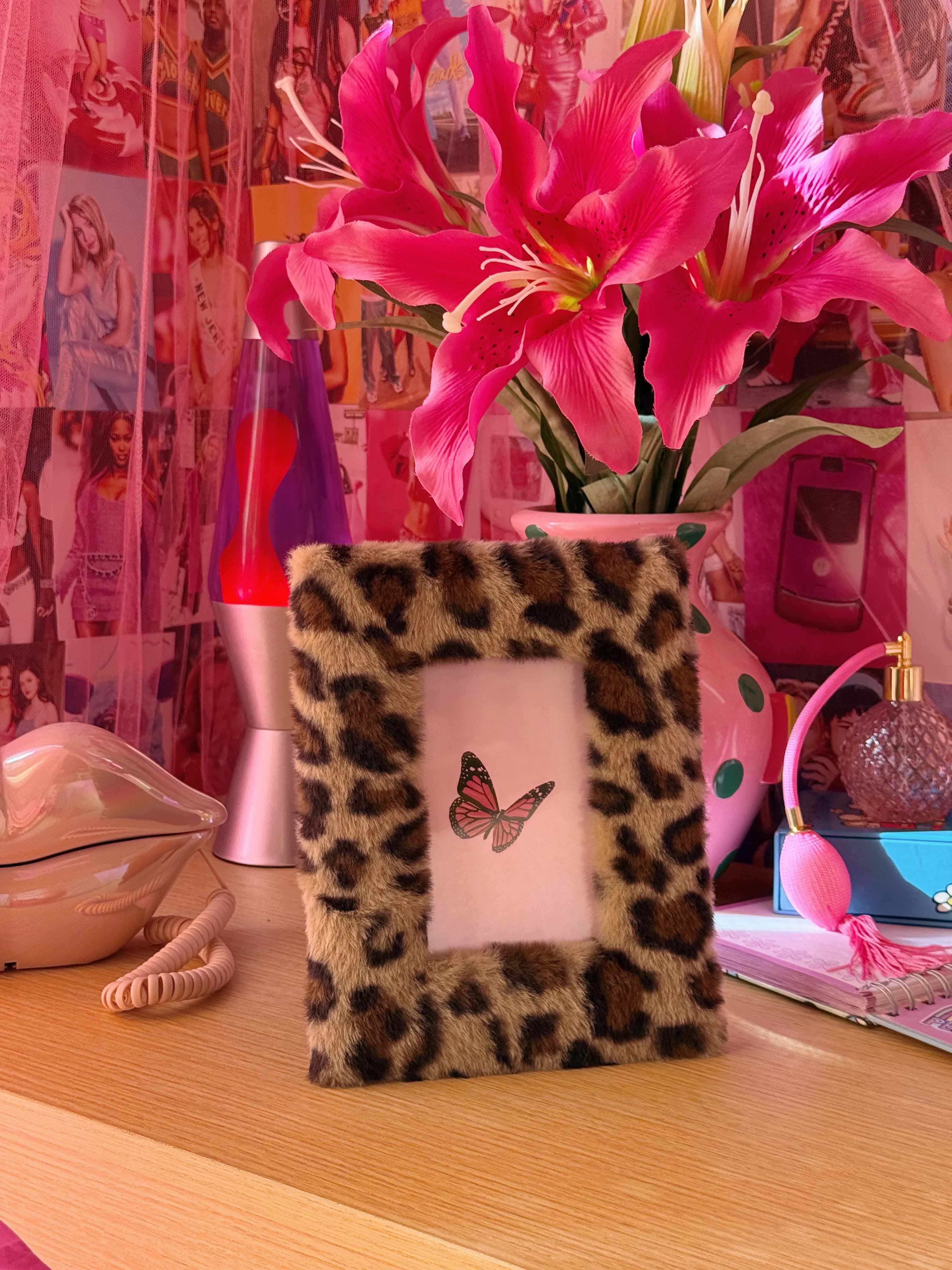 Leopard print photo frame with a butterfly on a desk with pink flowers and colorful decor.