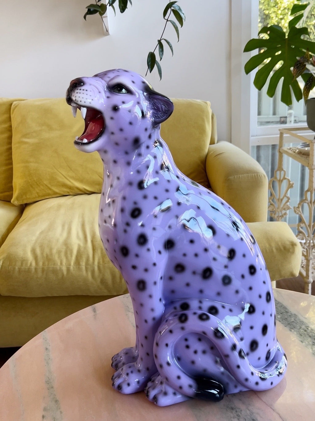 Purple leopard figurine on a table with a yellow couch and plants in the background