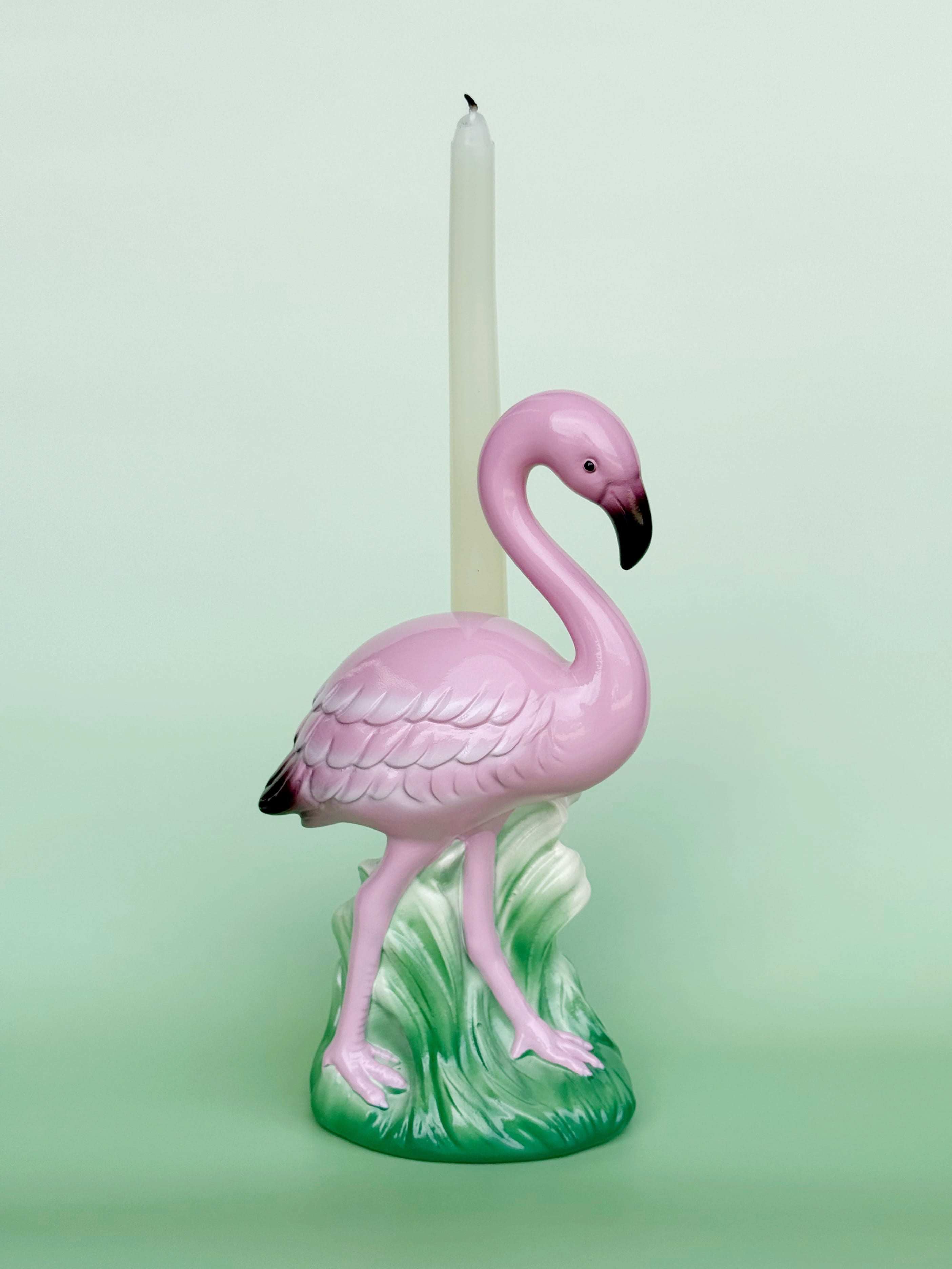 Pink flamingo candle holder with a white candle on a light green background