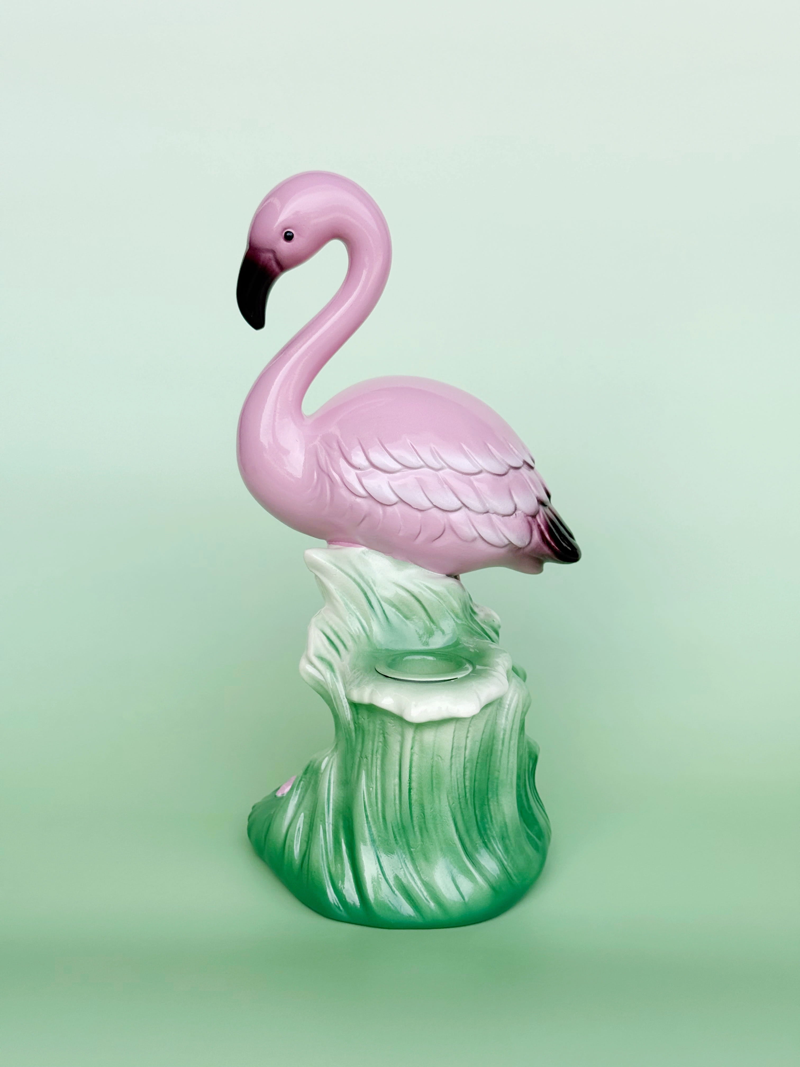 Pink flamingo figurine on a green base against a light green background