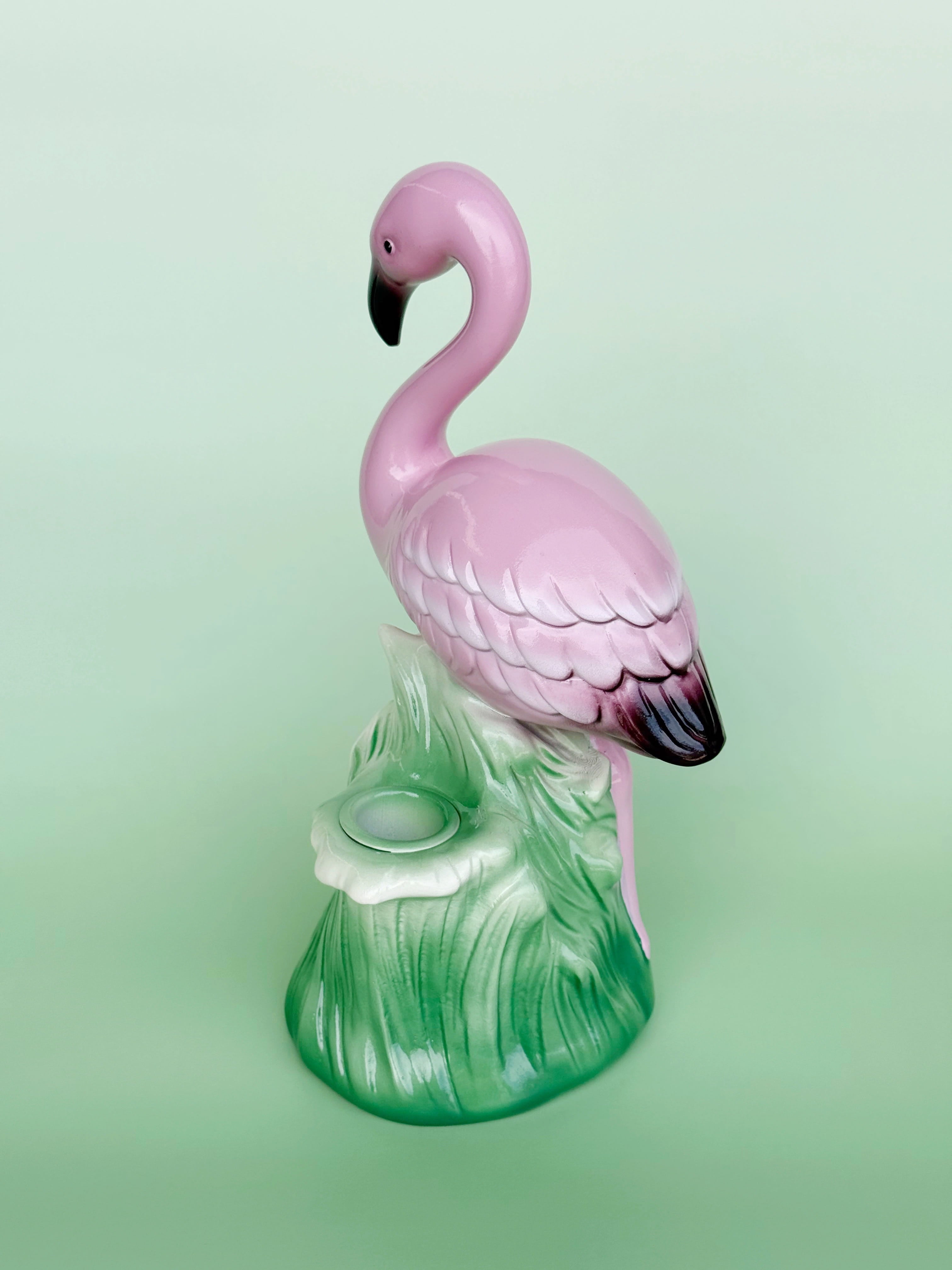 Pink flamingo figurine on a green base against a light green background