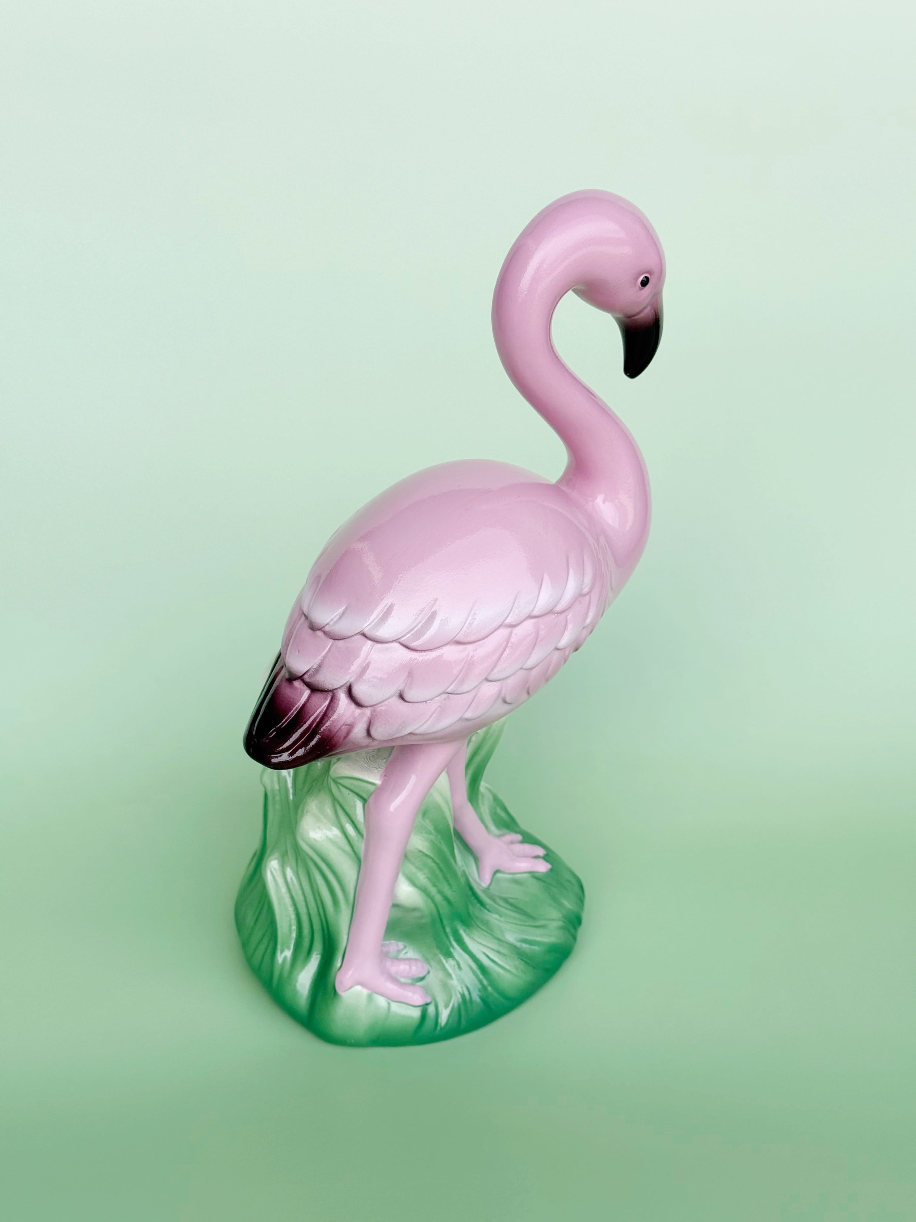 Pink flamingo figurine on a green base against a light green background