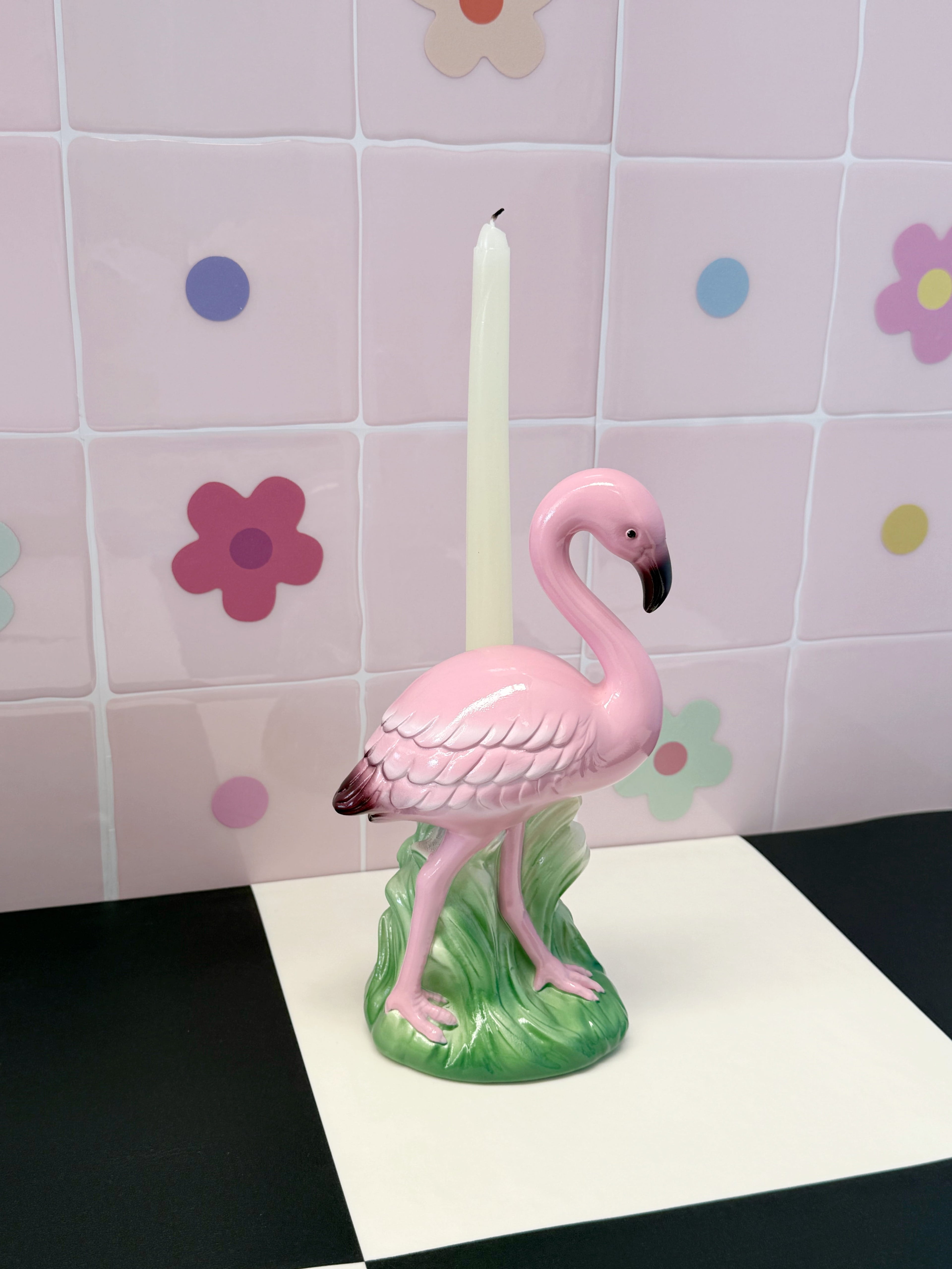 Pink flamingo candle holder with a candle on a tiled wall background