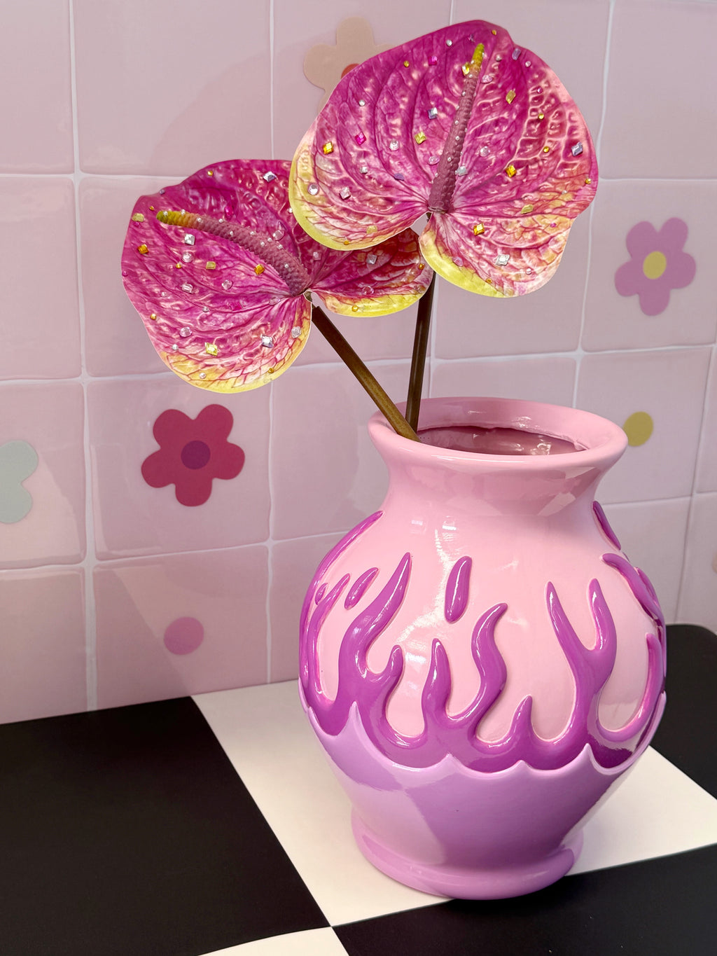 Pink vase with decorative flowers against a tiled wall background