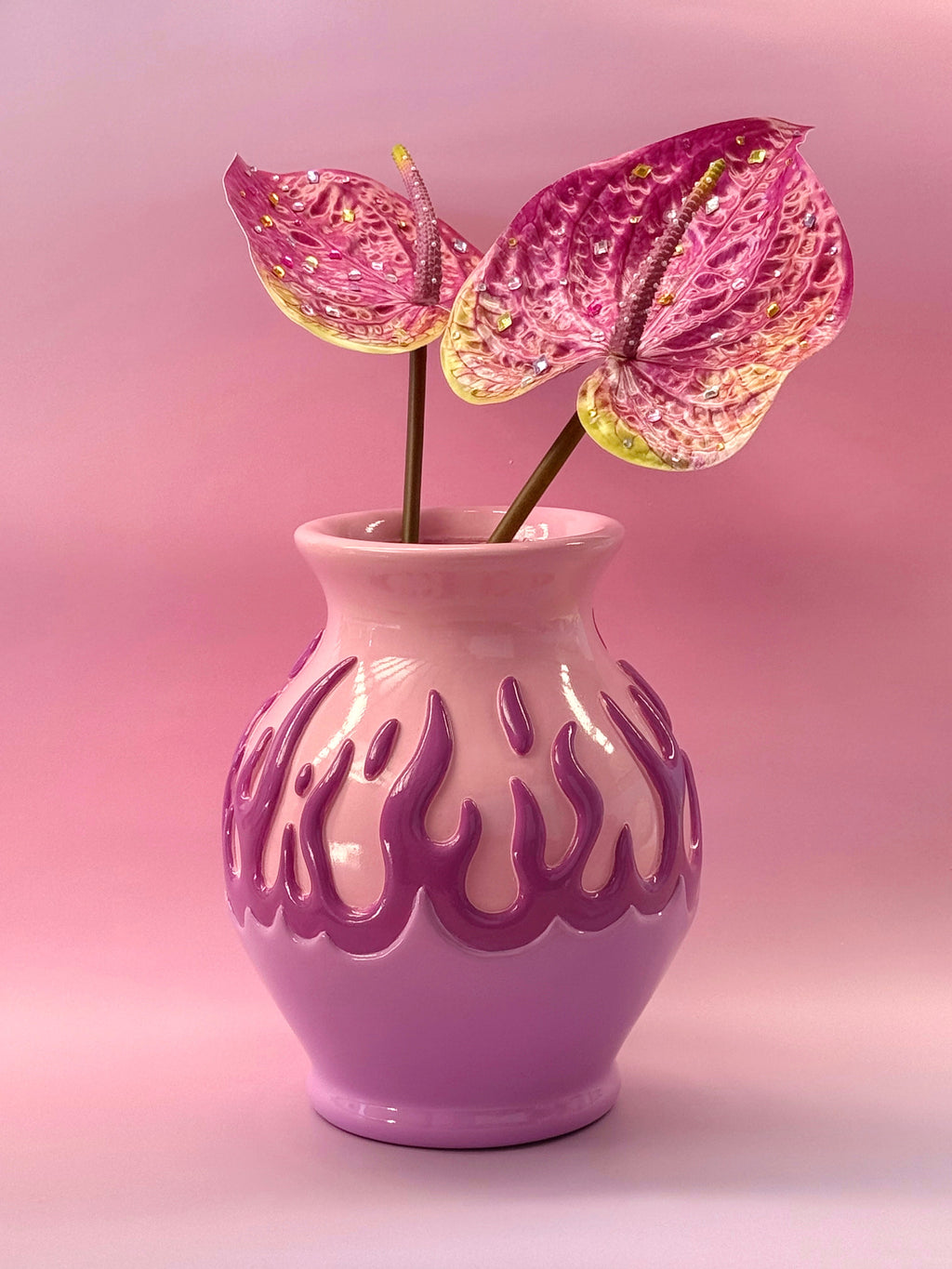 Pink vase with flame-like patterns holding pink flowers against a pink background