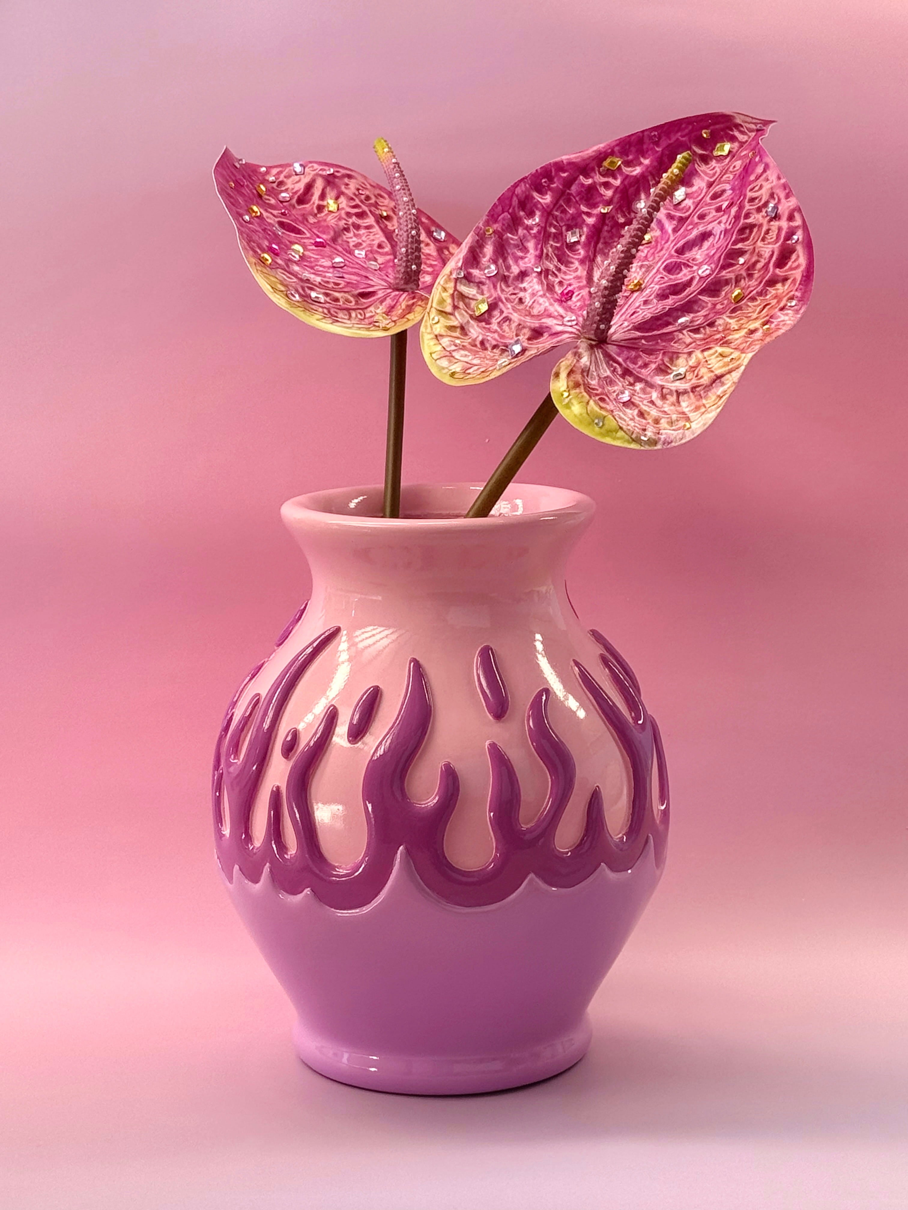 Pink vase with flame-like patterns holding pink flowers against a pink background