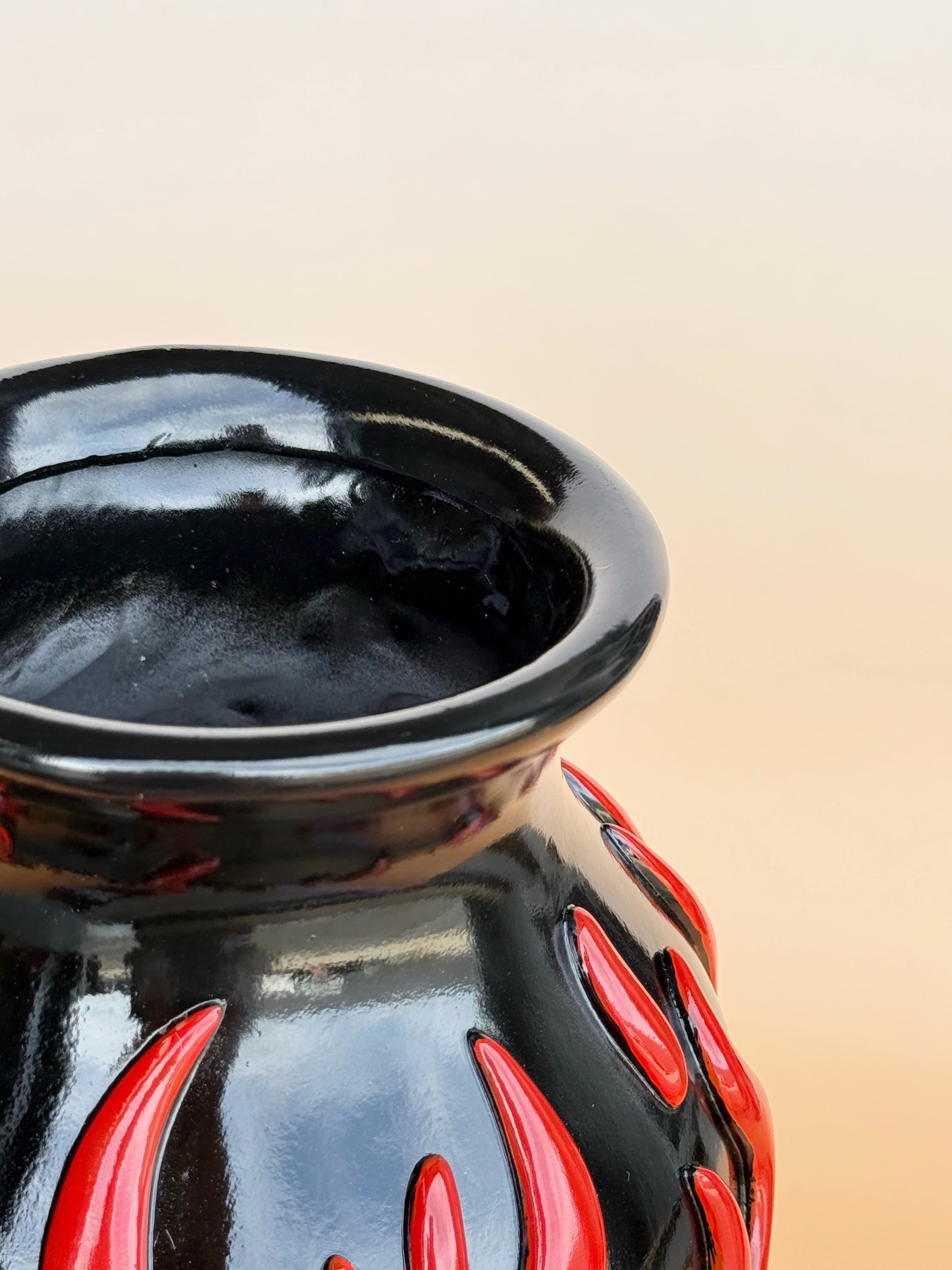 Black ceramic vase with red flame patterns on a beige background