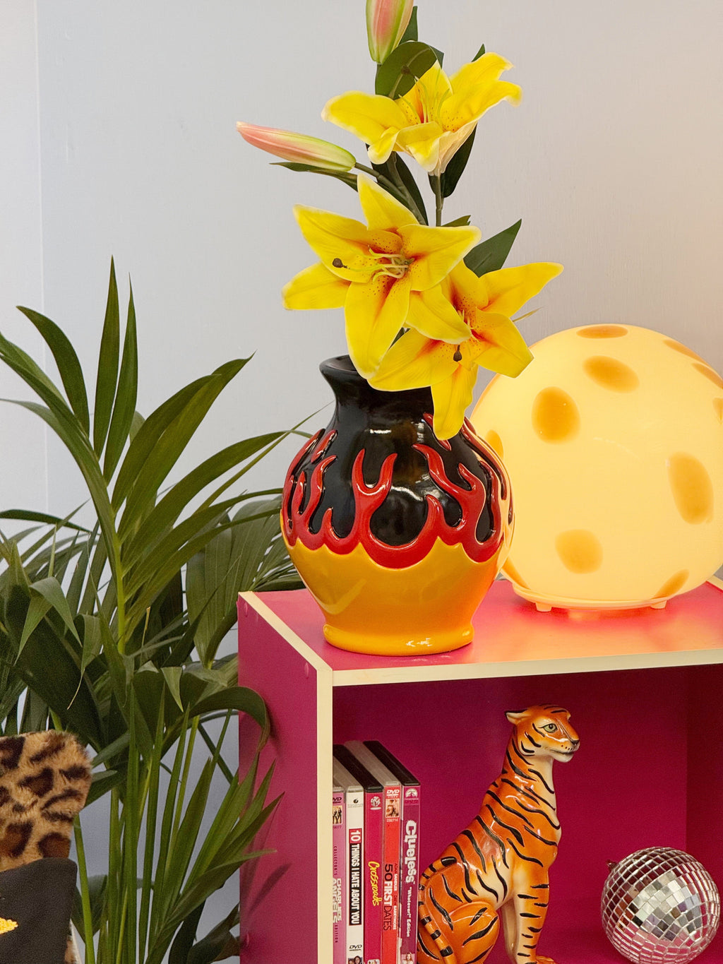 Vase with yellow flowers on a pink shelf next to a tiger figurine and plant