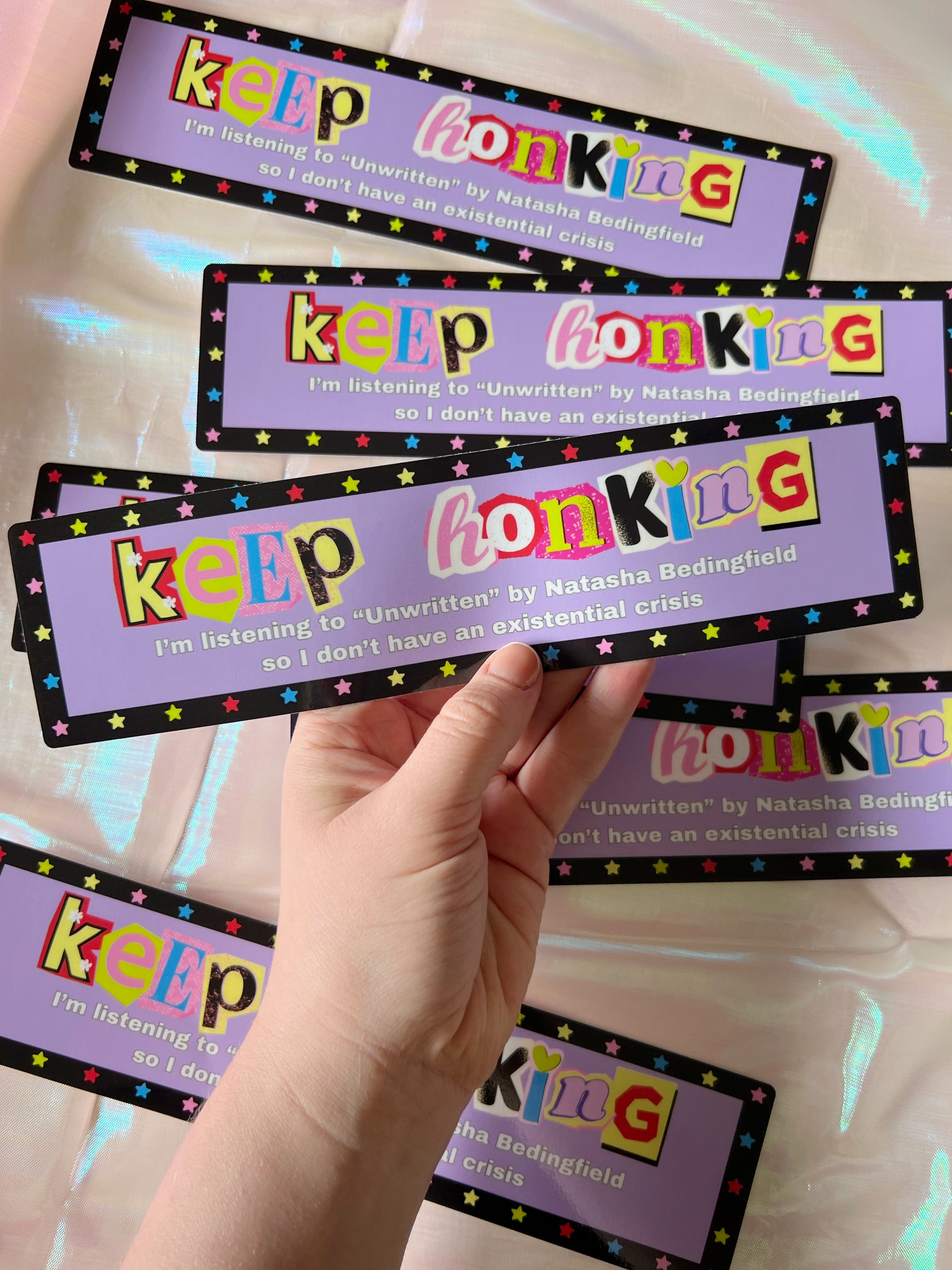 Photo of hand holding a bumper sticker that says "keep honking I'm listening to Unwritten by Natasha Bedingfield so I don't have an existential crisis" 