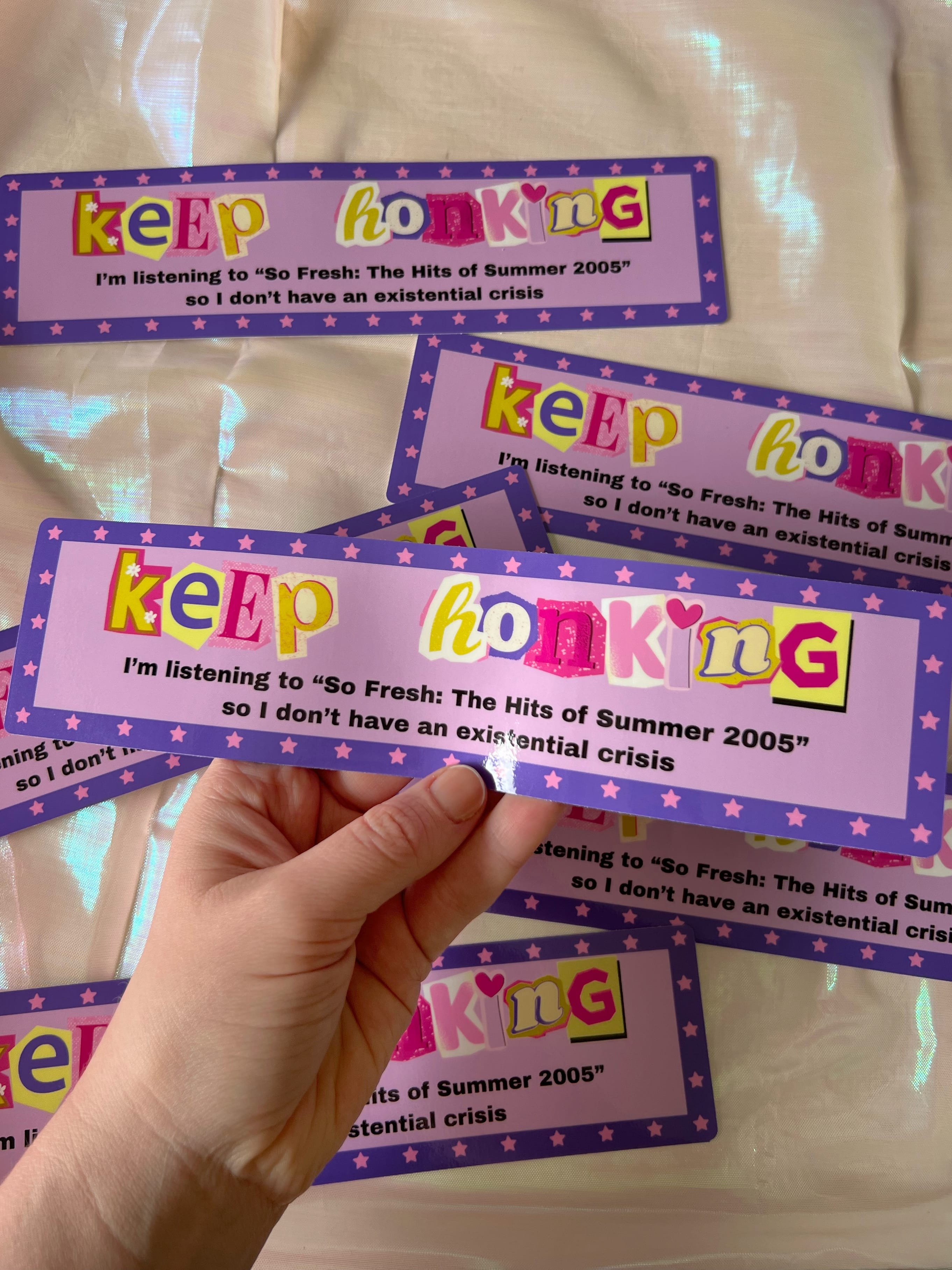 a hand holding a bumper sticker that says "keep honking I'm listening to the absolute masterpiece that is the Shrek 2 soundtrack"