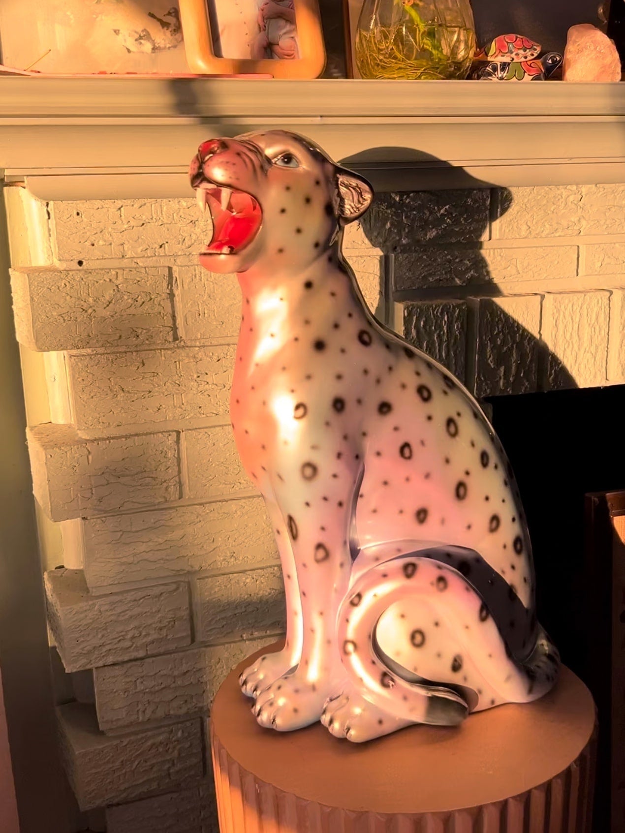 Decorative resin leopard figure with open mouth on a stand in front of a fireplace.
