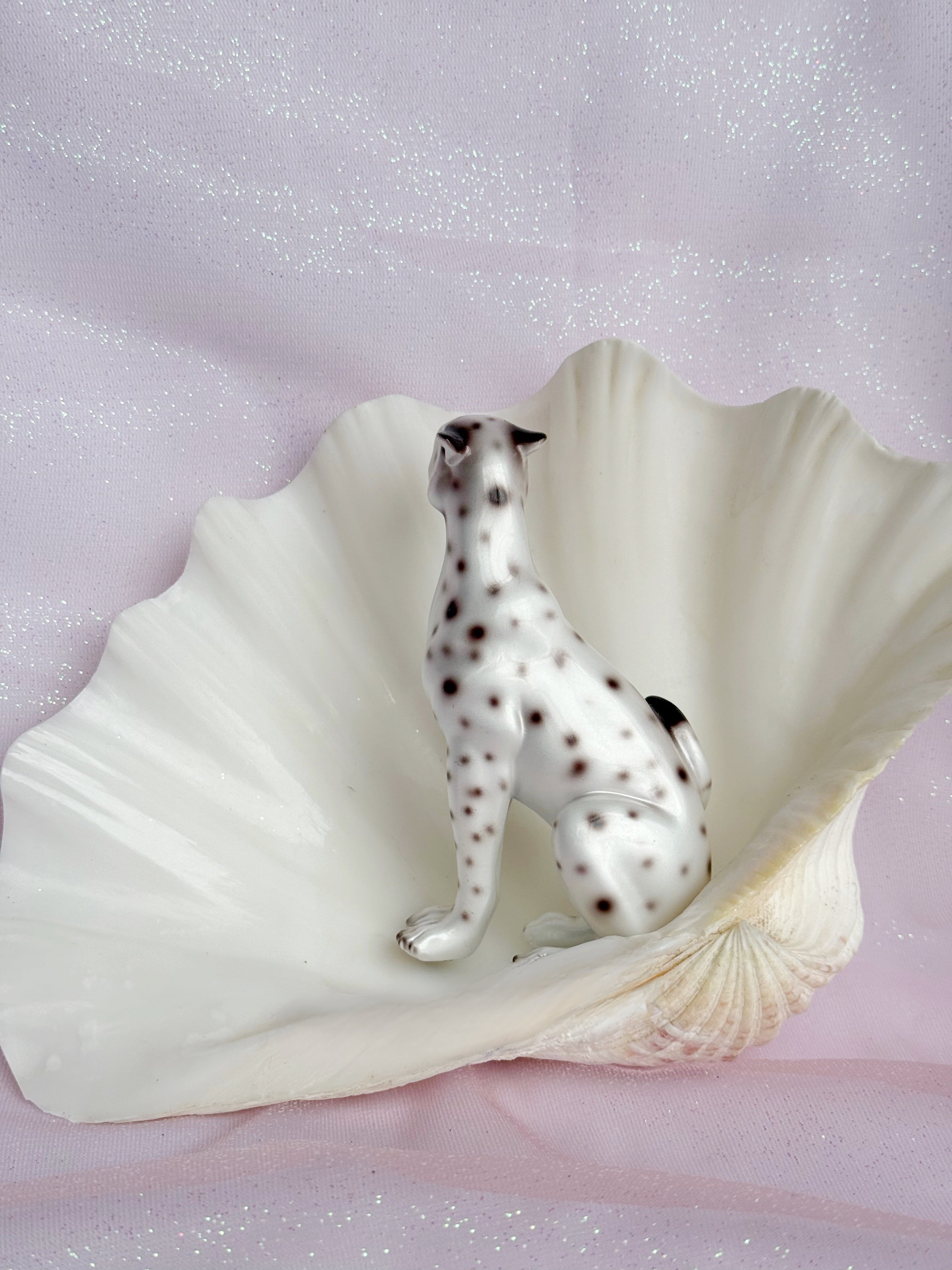 Leopard figurine inside a large shell on a glittery pink background