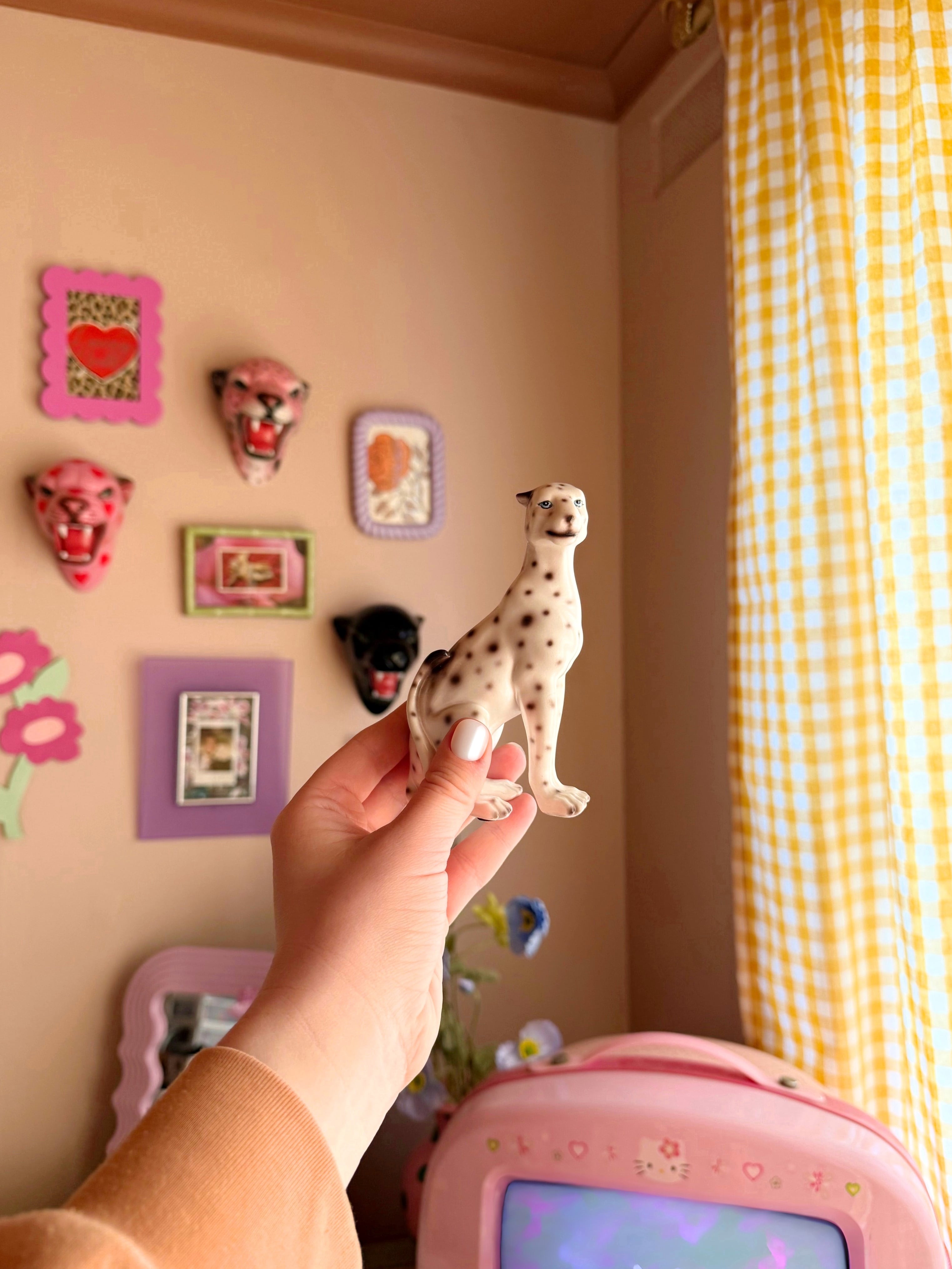 a hand holding a mini white leopard figurine with colourful home decor in the background