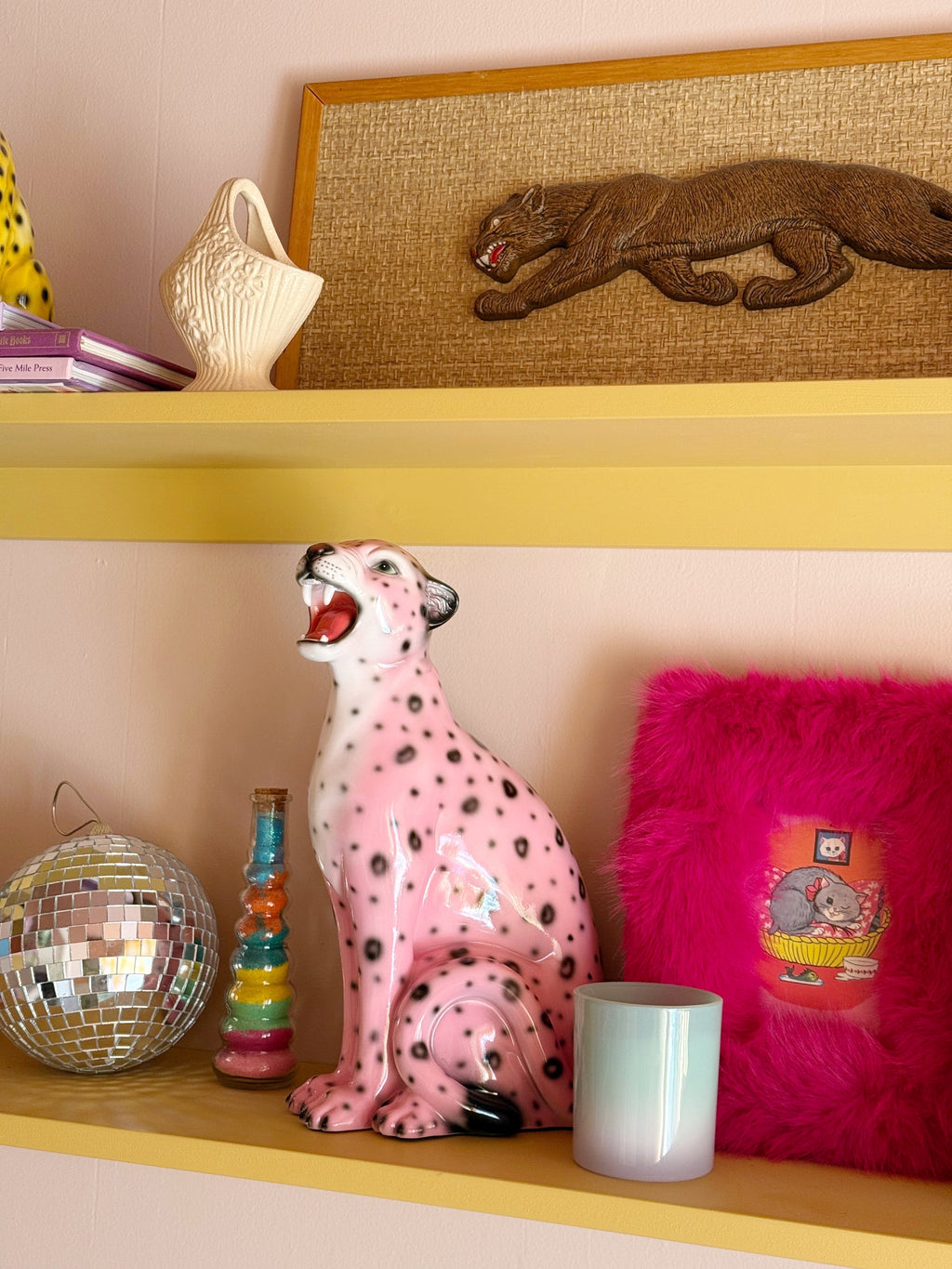 a small pink leopard figurine displayed on a shelf with other fun and quirky decor items