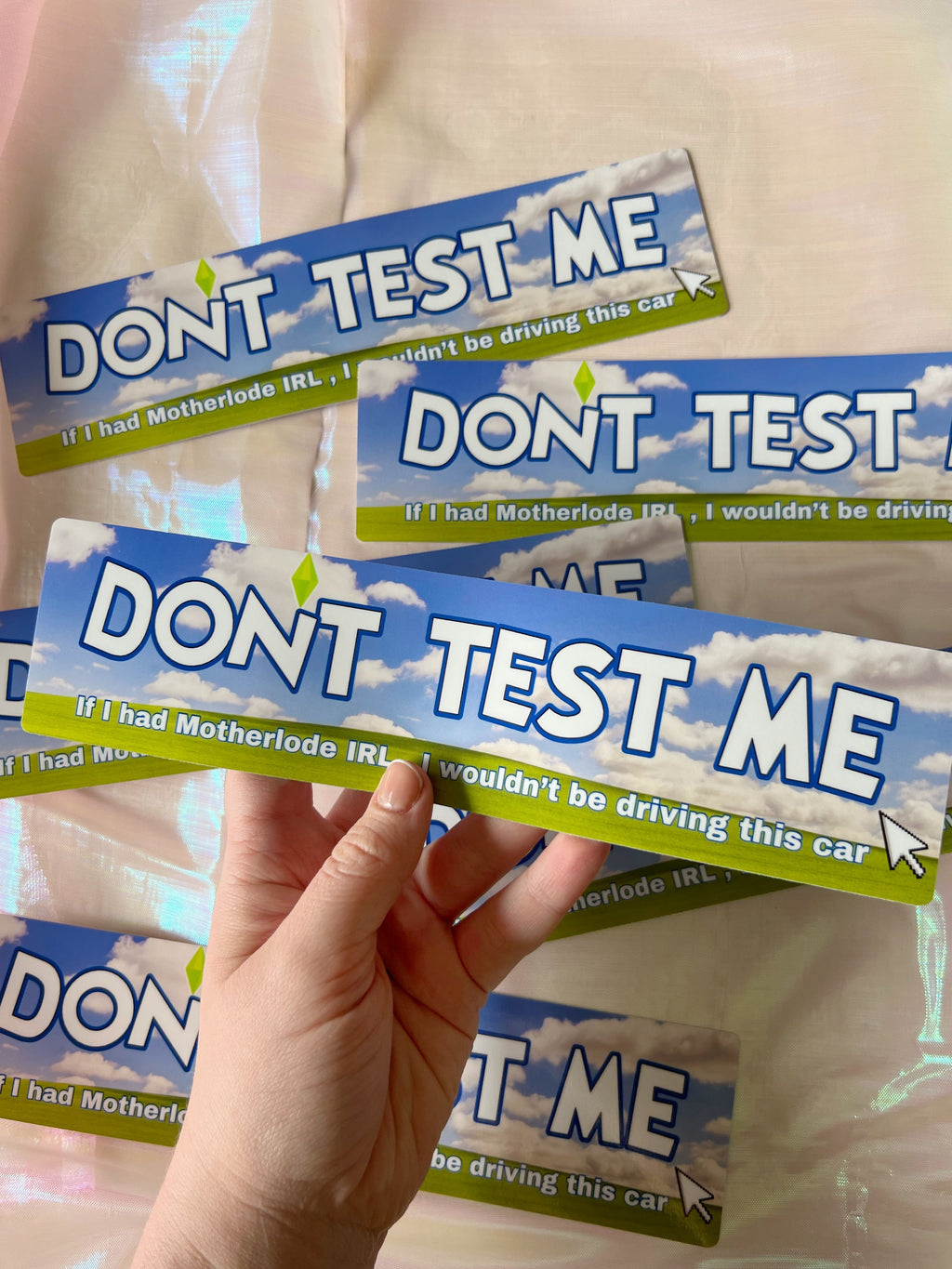 a hand holding a bumper sticker that says "don't test me if I had motherlode IRL, I wouldn't be driving this car"